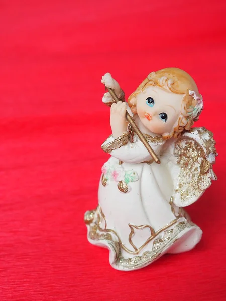 Guardian angel plays the flute. Figurine of a red-haired girl in a white dress with wings and a pipe. New Year or Christmas holiday background. Copy space. Pink background. Free space for text