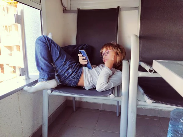 Letnia Biała Dziewczyna Leży Fotelu Balkonie Śmiejąc Się Trzymając Smartfona — Zdjęcie stockowe
