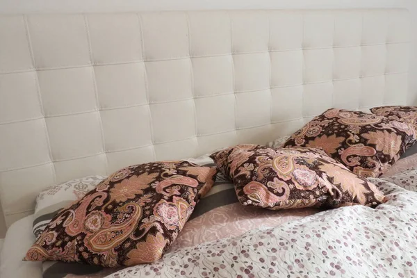 Pink decorative pillows on the bed linen. Double bridal bed with pillows and thick feather duvet. Bedroom design. Soft white headboard. Interior with furniture and bedding