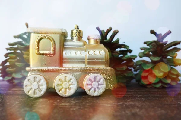 Golden children's toy train. Cones painted with green gouache as small Christmas trees. New Year or Christmas card. Icicles and snow on the train. Festive bokeh background. Christmas decorations.