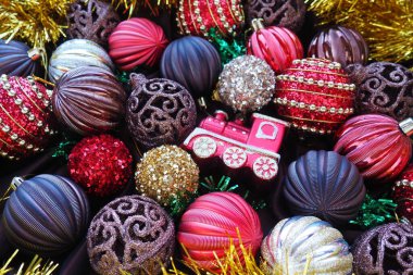 Sarı süslemeli ve Noel toplu Noel arkaplanı. Güzel Noel oyuncakları ve dekorasyonları. Kırmızı, altın, kahverengi, gümüş, sarı çizgili parlak toplar. Oyuncak trenin lokomotifi