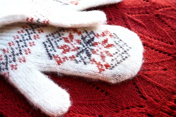 Fluffy white knitted mohair mittens with a traditional floral pattern on the back. A pair of mittens fashion accessories. Knitted with red and black threads geometric jacquard pattern. Winter clothes