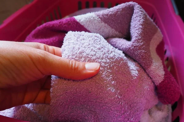 A woman's hand is feeling a cotton colored towel from a basket with dirty laundry. Laundry sorting and washing. Laundry room or bathroom. Housekeeping. Pink and blue terry towels