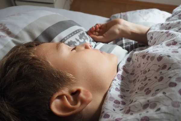 一个漂亮的高加索男孩 睡在床上 毛绒绒毛毯和枕头 晨阳的柔和光芒 耳朵特写 孩子在休息 健康的睡眠 — 图库照片