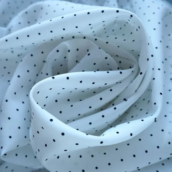Texture of silk fabric. Black polka dots on a white background. Dress lightweight synthetic fabric in white with a repeating pattern. The textile is made up of waves and folds. Feminine classic style
