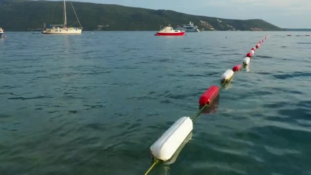 2022年8月13日 モンテネグロ メルジネ ボート ヨットが海に浮かぶ ブイはエリアマーカーを泳ぐ 耐久性を向上させるために耐久性のある白とマリンレッドエナメルでコーティングされた可視チャネルマーカー — ストック動画