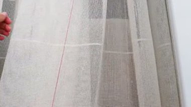 Beyaz pamuklu kumaş ya da ince ipliklerden örülmüş keten perdeler. Basit ekonomik apartman iç mimarisi. Odadaki pencere dekorasyonu. Bir kadın tülleri elle okşar, kalitesini gösterir.