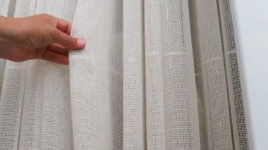 Beyaz pamuklu kumaş ya da ince ipliklerden örülmüş keten perdeler. Basit ekonomik apartman iç mimarisi. Odadaki pencere dekorasyonu. Bir kadın tülleri elle okşar, kalitesini gösterir.