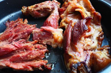 Roasted smoked pork shoulder or knee. Delicious meat on a black baking sheet with drops of vegetable oil, taken out of the oven. Pork delicacy for dinner in a restaurant and family lunch. Red meat.