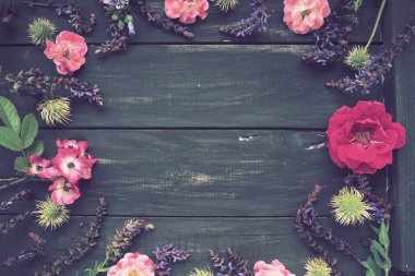 Ahşap bir arka planda daire şeklinde çiçekler. Tatil için kartpostal. Güller, sardunyalar, lavantalar, adaçayı ve kıllı kestaneler koyu tahtaların kenarlarına yerleştirilir. Arkaplan kopyalama alanı, düz uzanma