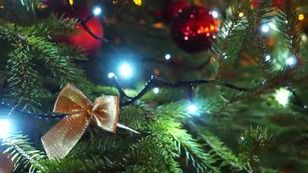 枝に赤いガラスボールで幸せな新年のクリスマスツリーの装飾 家族の休日のために電球のガーランドをちらつき側のボケ お祭り気分 紙や布でカットされた弓やパターン — ストック動画