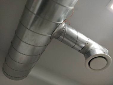Umumi tuvalette çıkarıcı kaput. Gri hava çıkarıcılı yuvarlak metal boru. Mühendislik havalandırma sistemleri. Odanın tavanının altındaki galvanize borular. Plastik yuvarlak uç.
