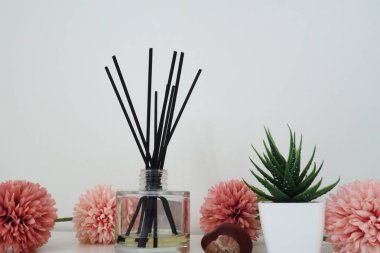 Pembe yapay çiçeklerin bileşimi, tütsü vazoya yapışmış vazo ve gerekli yağ. Beyaz bir masada hala hayat var. Aloe çiçeği beyaz tencerede. Oda ve apartman dekorasyonu, iç tasarım.