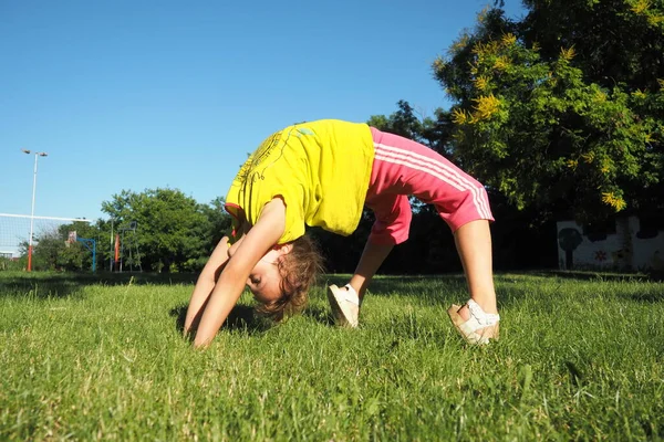 Caucasian girl 8 years old doing a bridge exercise on the grass in the park. Playground. Childrens sports. Spine health, treatment of scoliosis.