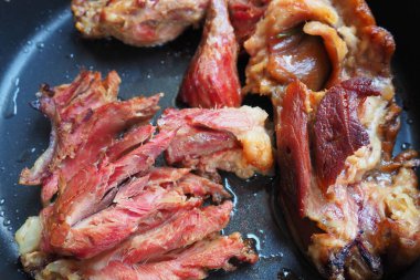 Roasted smoked pork shoulder or knee. Delicious meat on a black baking sheet with drops of vegetable oil, taken out of the oven. Pork delicacy for dinner in a restaurant and family lunch. Red meat.