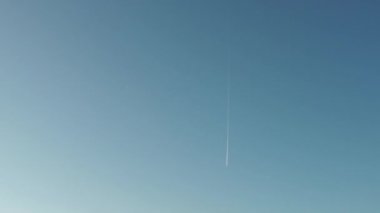 Mavi gökyüzünde uçarken parlak beyaz bir iz bırakan bir jet uçağı. Grafik ve seyahat videoları için arka plan. Gökyüzü açık