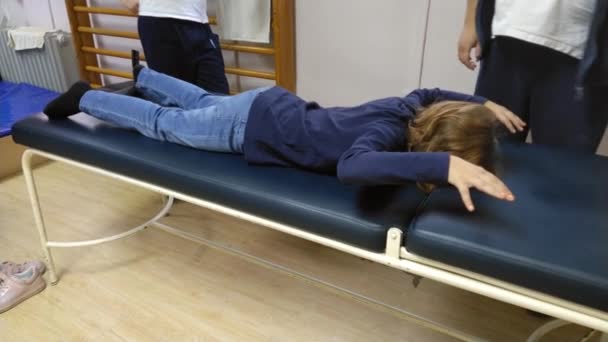 理疗师对女孩进行脊柱侧弯训练 展示她在反脊柱侧弯体操过程中的练习 这个孩子在沙发上进行体育锻炼 把胳膊向后弯 把她的身体抬起来 — 图库视频影像