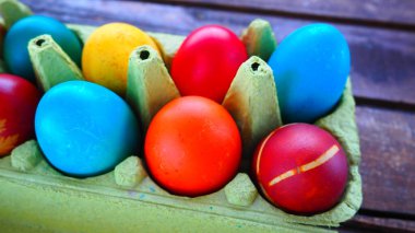 Multi-colored eggs painted with gouache and onion peel in a cardboard box on a wooden table background. Ten boiled eggs. Postcard poster for Easter. Easter holiday. Red, blue, yellow, brown eggs.