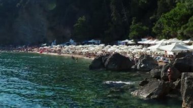 Budva, Karadağ, Mogren plajı. 15 Ağustos 2022. Yüksek kayalıkların yakınındaki kum ve çakıl taşı plajı. Plaj şemsiyeleri, kafeler, şezlonglar, şezlong. İnsanlar rahatlar, yüzer, güneşlenir. Kız poz veriyor.