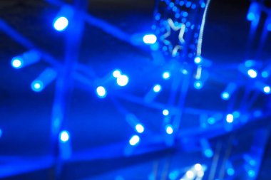 Mavi sokak çelenkleri. Odaklanmış bokeh. Şenlik arka planı. Yeni yıl ve Noel gecesi süslemesi olarak mavi ve beyaz ampuller. Sokak dekorasyonu. Soyut ışık noktaları. Yıldız şekli.