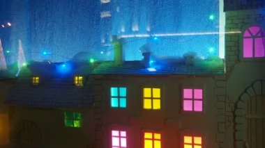 Theatrical showcase with a cute childrens winter New Years town. Houses with colored windows. Flashing holiday garlands. The glare of car headlights is reflected in the glass. Christmas decorations.
