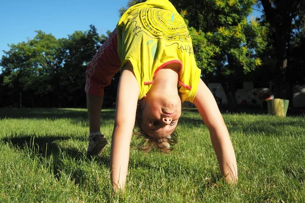 Caucasian girl 8 years old doing a bridge exercise on the grass in the park. Playground. Childrens sports. Spine health, treatment of scoliosis.