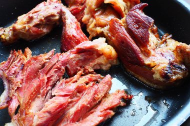 Roasted smoked pork shoulder or knee. Delicious meat on a black baking sheet with drops of vegetable oil, taken out of the oven. Pork delicacy for dinner in a restaurant and family lunch. Red meat.