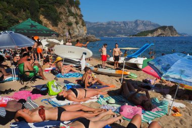 Budva, Montenegro, Mogren beach. August 15 2022 Sand and pebble beach near high cliffs. Beach umbrellas, cafes, deck chairs. People relax, swim, enjoy and sunbathe. Tourism business in the Balkans