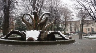 Sremska Mitrovica Serbia 01.27.2023 City Fountain Stone flower in the central park. Snow and cloudiness in winter. Passers-by go, cars go. Two young people passed by. A man is passing by on a bicycle