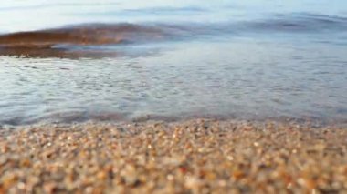 Waves of clear water crash on sandy beach. Golden hour, sunset. Rest on the ocean, sea, lake or river. Ripples on the water. Appearing disappearing shadow of a child. Coarse sand, bubbles and splashes