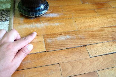 Çizilmiş eski parke döşeme bakım gerektiriyor. Parke, uzun süreli kullanımdan kaynaklanan çizikler yüzünden zarar görmüş. Uzman eller zeminde hasar olduğunu gösteriyor. Antika tahta bir yatağın bacağı..