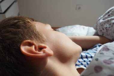 8 yaşında, güzel, beyaz, sarı saçlı, yumuşak bir battaniye ve yastıkla yatakta uyuyan bir çocuk. Sabah güneşinin yumuşak ışığı. Kulak arkası. Çocuk dinleniyor. İyi uykular.