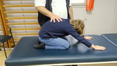Fizyoterapist skolyoz hastası bir kızı eğitiyor. Egzersizlerini skolyoz karşıtı jimnastik kursundan gösteriyor. Çocuk fiziksel egzersiz yapıyor. Sırt kaslarının gevşemesi ve gerilmesi.