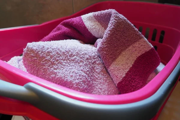 Towels in the laundry basket. Blue and pink cotton terry towels are thrown into a pink plastic basket. Housekeeping. Storing and separating laundry before washing. Light from above from an open window