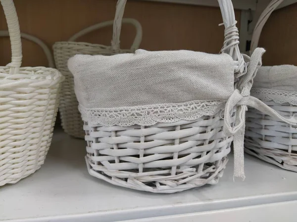 Wicker decorative baskets on a shelf in a store. Pretty baskets painted white. Textile bag. Stylish gift for Easter. Decor element of the interior of an apartment, a country house or a spring garden