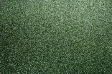 Deep grassy green. Texture of rough paper or cardboard. Defocused bokeh sparkles and shine on the fold. Festive green background with illuminated gradient from top right