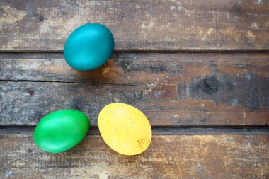 Multi-colored eggs painted with gouache and onion peel close up on wooden background. Three boiled eggs. Postcard poster for Easter. Easter holiday. Blue, yellow, green eggs.
