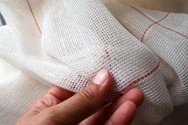 White coarse cotton or linen curtains made of weaves of thin threads. A womans hand is feeling the fabric. Window decoration room. Red stripe. The fabric is folded in soft waves. Apartment interior