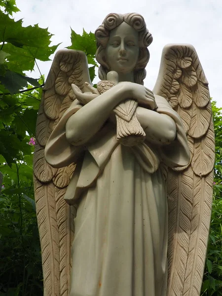 An angel with a dove. Sculpture in the cemetery. The figure of an angel with wings holding a bird in his arms. Lamentation for the deceased. Headstone monument on a Christian grave. Sadness sorrow