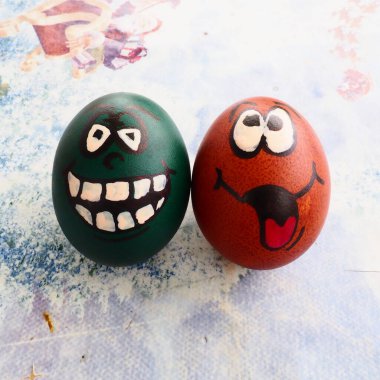 Easter eggs dyed green and brown with painted laughing faces. Funny grimaces with eyes, tongue and big white teeth. Scary face for Halloween. Emoticon for Easter. Light abstract background