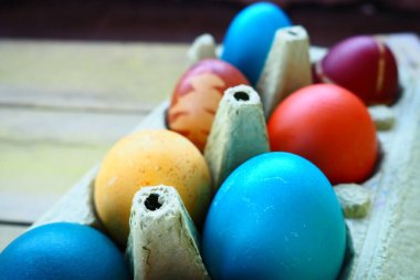 Multi-colored eggs painted with gouache and onion peel in a cardboard box on a wooden table background. Ten boiled eggs. Postcard poster for Easter. Easter holiday. Red, blue, yellow, brown eggs.