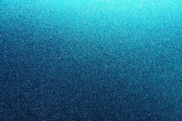 Deep blue. Texture of rough paper or cardboard. Defocused bokeh sparkles and shining. Festive blue background with illuminated gradient from top right. Deep blue sapphire