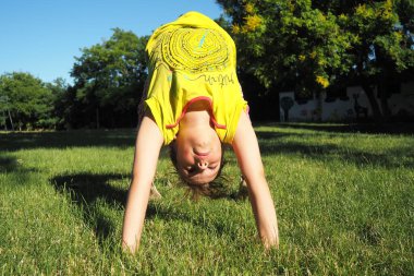 Caucasian girl 8 years old doing a bridge exercise on the grass in the park. Playground. Childrens sports. Spine health, treatment of scoliosis.