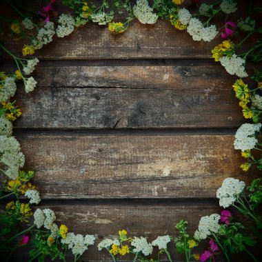 multicolored wildflowers are arranged in a circle on a wooden table background. White yarrow inflorescences, yellow grass mouse peas, pink ivy geranium. Horizontal boards. Romantic rustic style