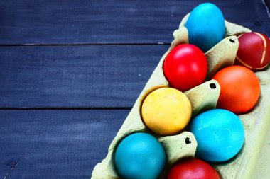 Multi-colored eggs painted with gouache and onion peel in a cardboard box on a wooden table background. Ten boiled eggs. Postcard poster for Easter. Easter holiday. Red, blue, yellow, brown eggs.