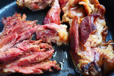Roasted smoked pork shoulder or knee. Delicious meat on a black baking sheet with drops of vegetable oil, taken out of the oven. Pork delicacy for dinner in a restaurant and family lunch. Red meat.