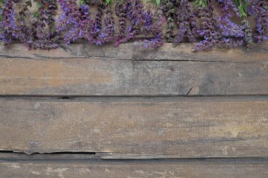 Ahşap bir masa üzerinde lavanta ve adaçayı çiçekleri. Mor ve mavi çiçekleri ve kenarlarında yaprakları olan eski ve koyu renkli tahtalardan oluşan yatay tahtalar. Durgun bir hayat ve düz bir hayat. Metin için boş kopyalama alanı. 