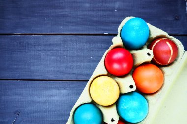 Multi-colored eggs painted with gouache and onion peel in a cardboard box on a wooden table background. Ten boiled eggs. Postcard poster for Easter. Easter holiday. Red, blue, yellow, brown eggs.