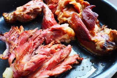 Roasted smoked pork shoulder or knee. Delicious meat on a black baking sheet with drops of vegetable oil, taken out of the oven. Pork delicacy for dinner in a restaurant and family lunch. Red meat.
