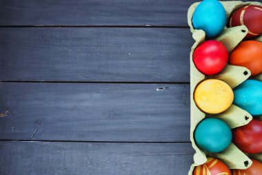 Multi-colored eggs painted with gouache and onion peel in a cardboard box on a wooden table background. Ten boiled eggs. Postcard poster for Easter. Easter holiday. Red, blue, yellow, brown eggs.